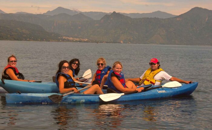 A group of women and a young man kayaking on the serene waters of Lake Atitlán, showcasing the safe and enjoyable travel experiences available in Guatemala.