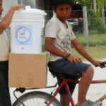 Two young men transport the Ecolfilter on their bicycle as part of the Pure Water Pathways Program, a sustainable initiative by Martsam Travel.